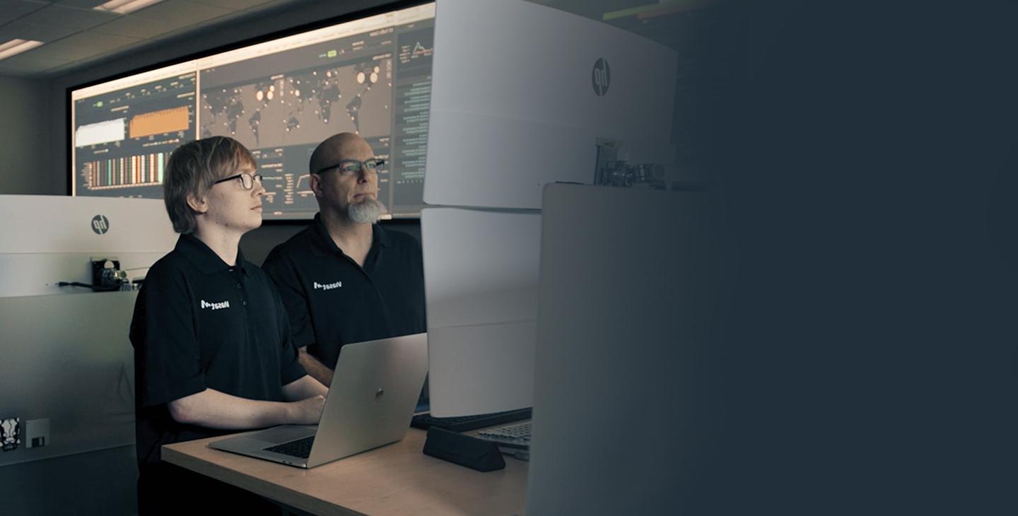 两名身穿带有白色Viasat标志的黑色polo衫的男性Viasat员工在网络安全运营中心工作