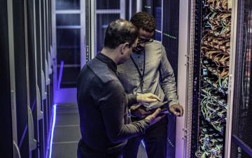 2 men in a server room discussing space communications and looking at a tablet