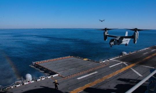 Two loarge military planes approaching a landing pad on a ship at sea